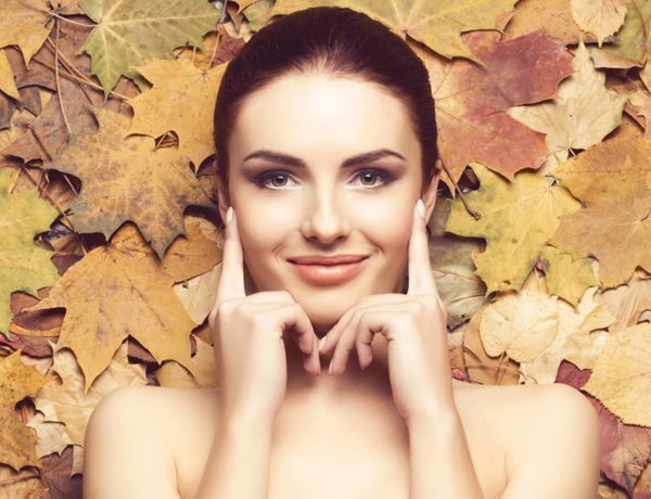 Eine Frau mit freundlichem Lächeln auf einem herbstlichen Hintergrund mit getrockneten Blättern.