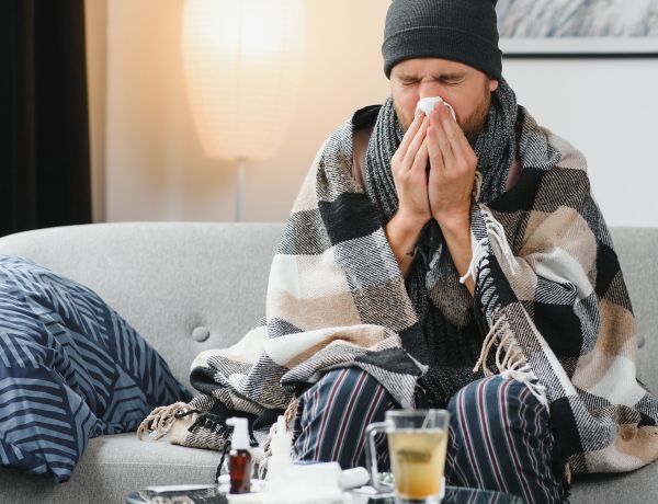 Mann krank auf Sofa mit Decke und Taschentuch