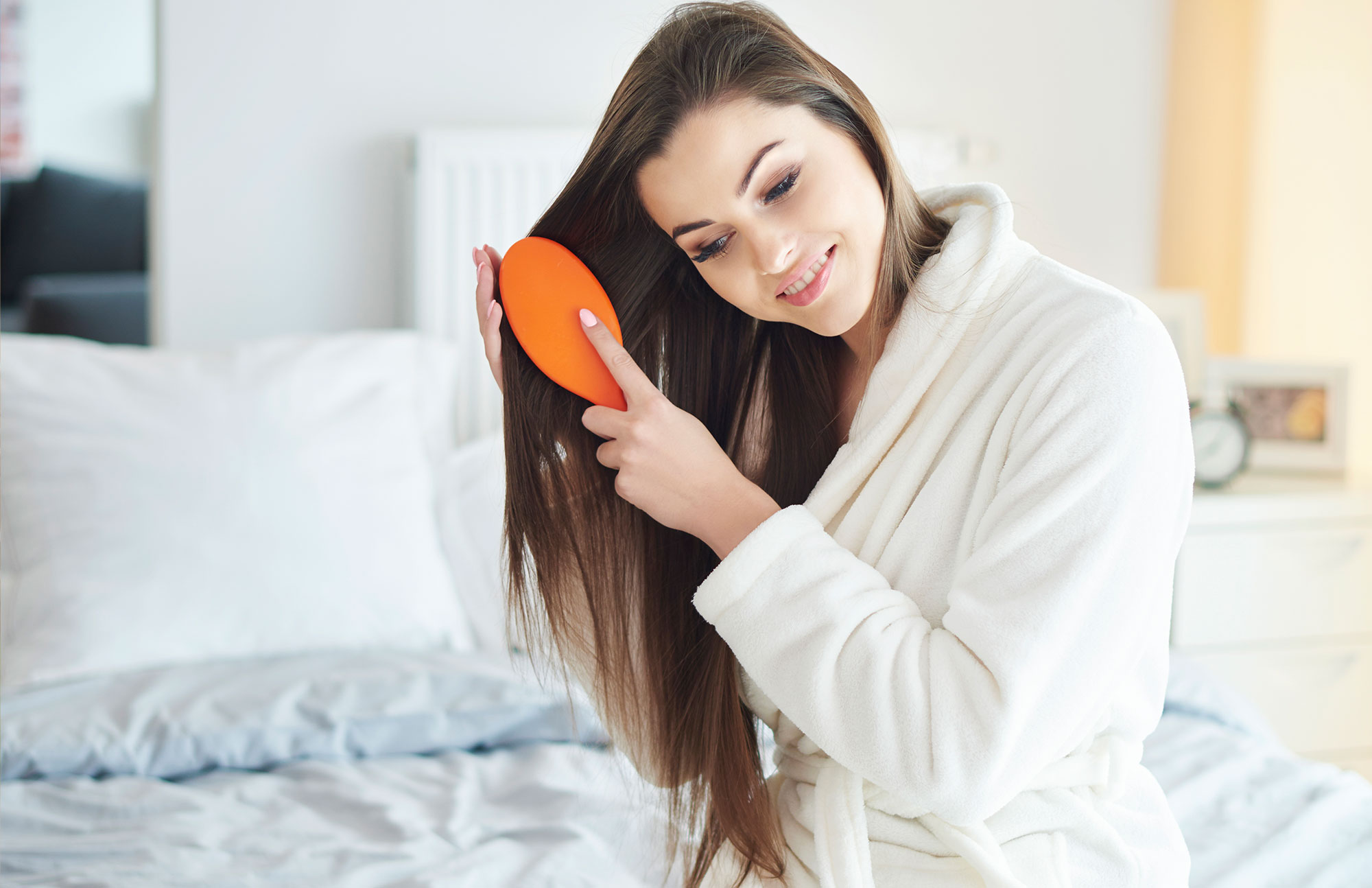 Frau mit langen Haaren sitzt auf dem Bett und kämmt sich.