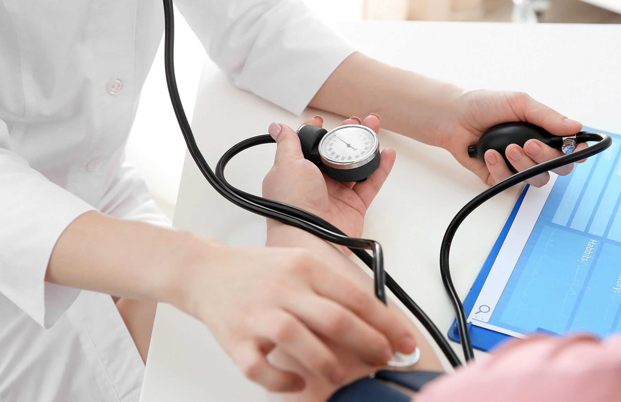 Hände messen mit Blutdruckmanschette den Blutdruck einer Person am Tisch.