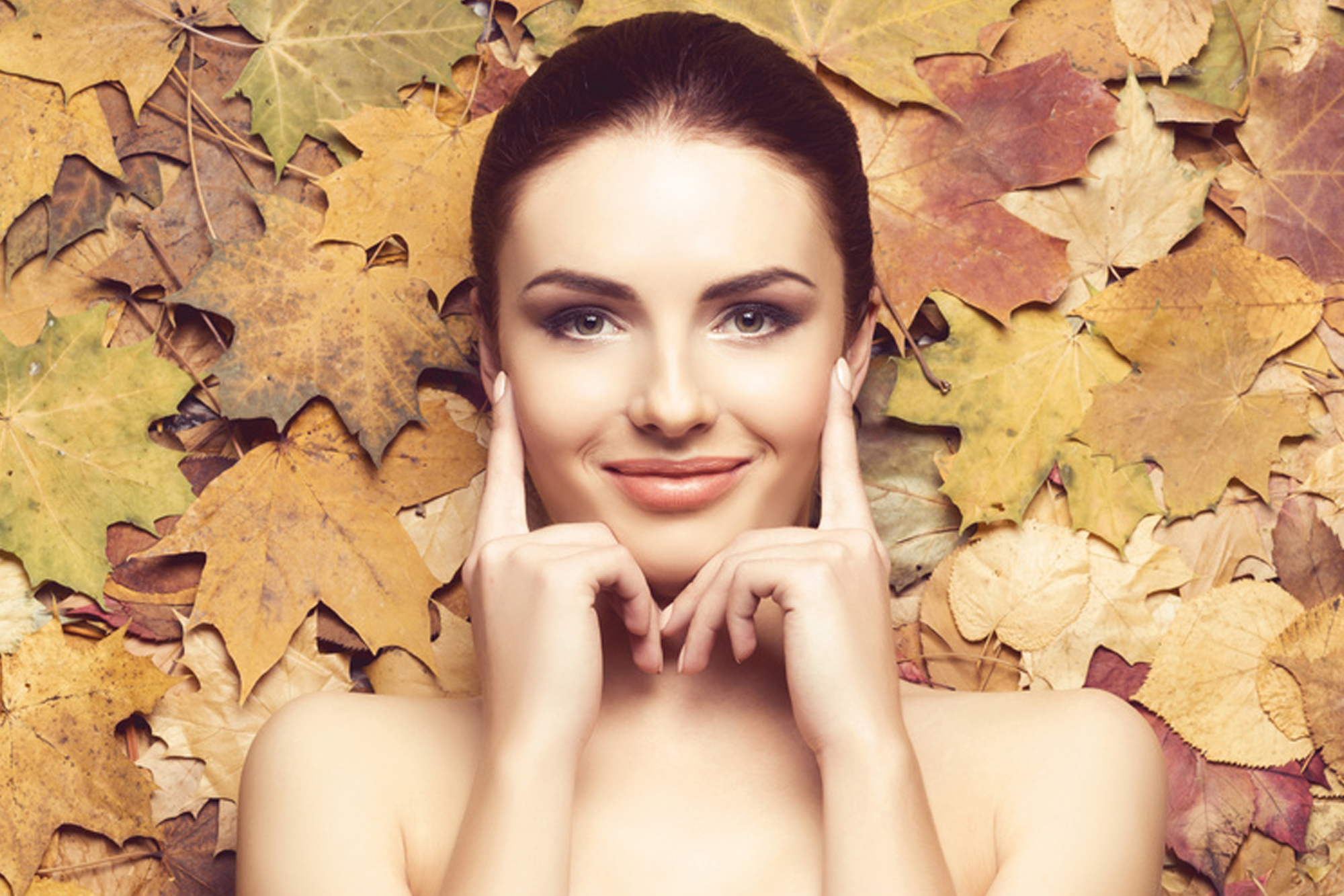 Eine Frau mit freundlichem Lächeln auf einem herbstlichen Hintergrund mit getrockneten Blättern.